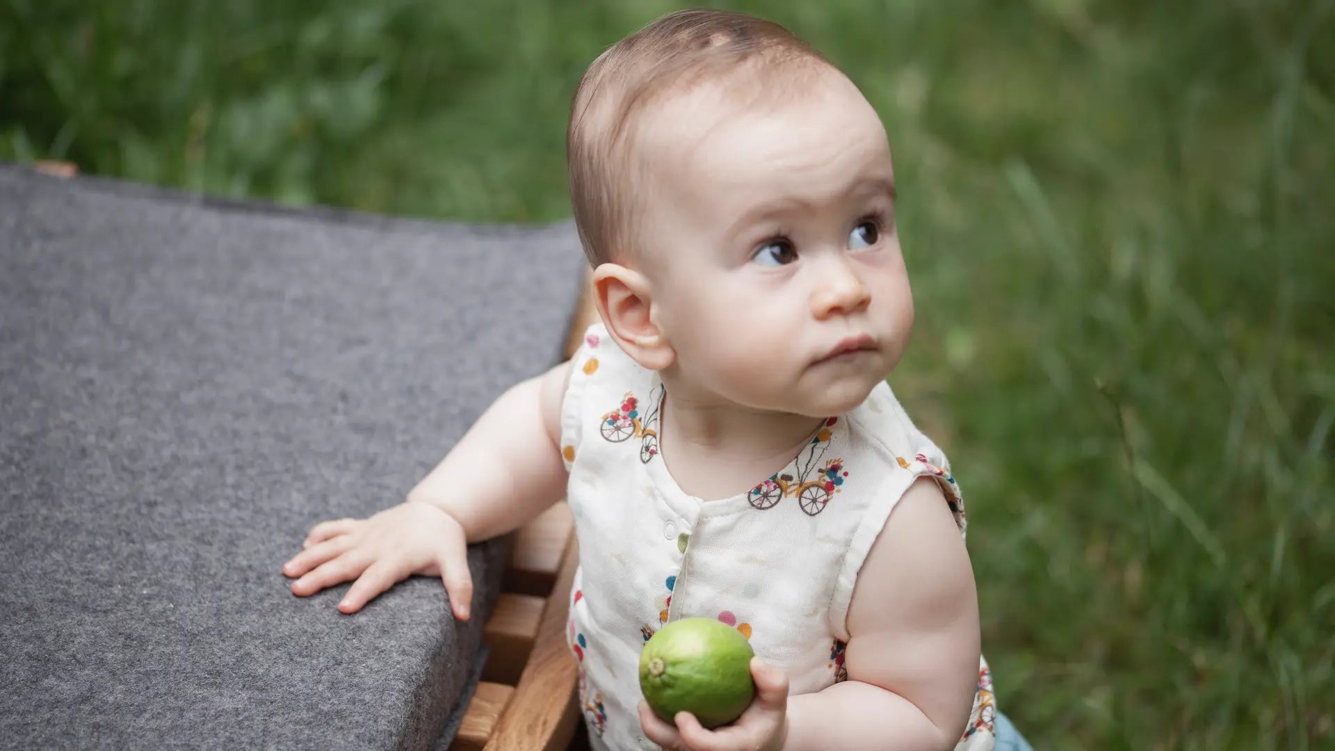 Baby steht auf der grünen Wiese im Garten mit einer grünen Limone in der Hand.