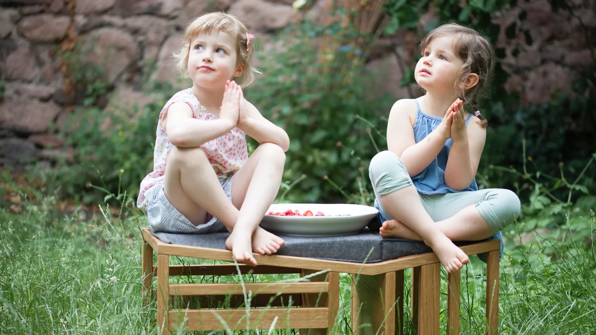 Zwei Kinder, die nebeneinander auf einer Sitzbank aus Eichenholz im Garten sitzen.