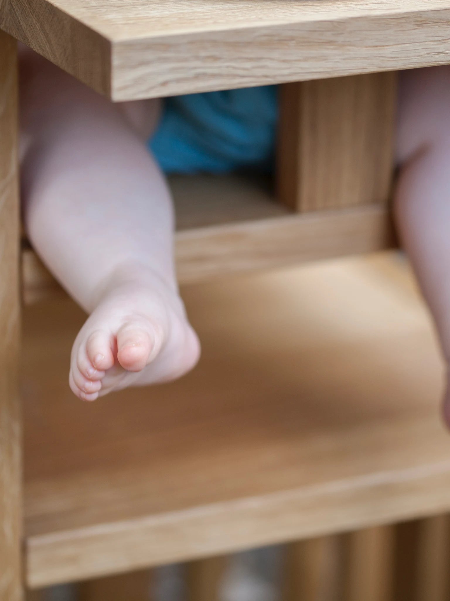 Der ZAUNKÖNIG Lernturm (3-in-1) aus massivem Eichenholz als Hochstuhl im Garten; Detailansicht mit Bein und Fuß eines Kindes.
