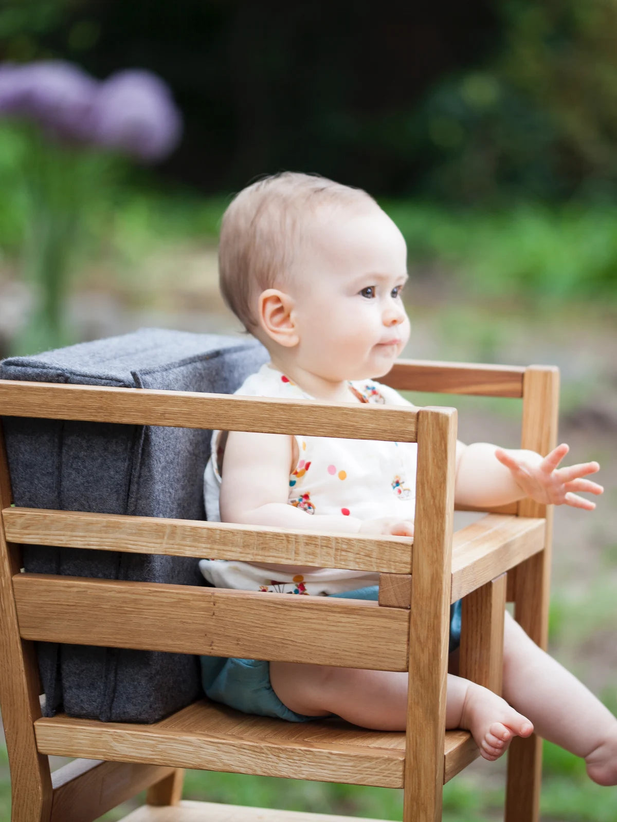 Der ZAUNKÖNIG Lernturm (3-in-1) aus massivem Eichenholz als Hochstuhl im Garten mit Faltpolster als Rückenlehne und Rausfallschutz; Seitenansicht mit Kind.