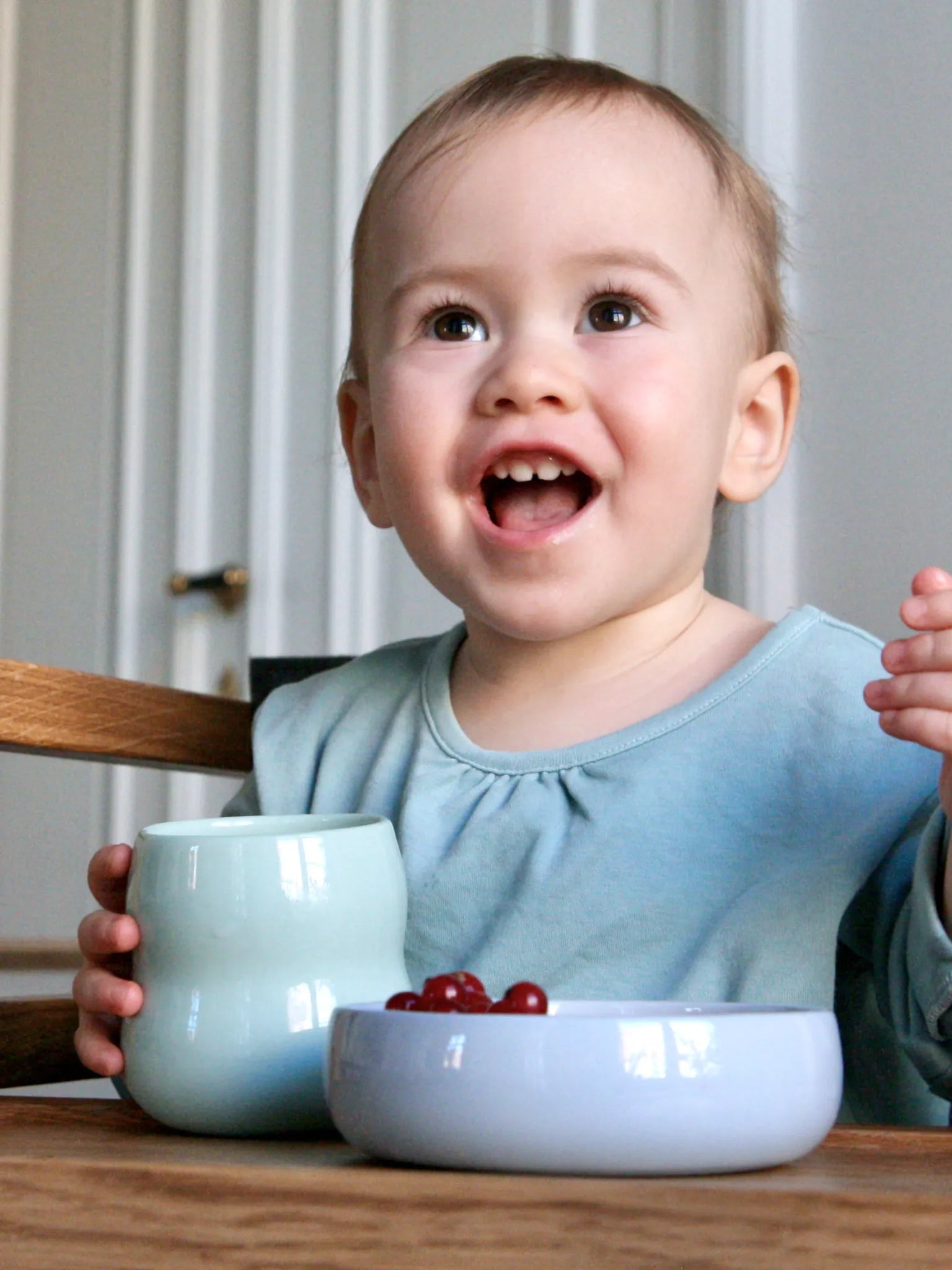 Kind mit Kindergeschirr aus Porzellan, Frontansicht des Kinderbechers in Agave und der Kinderschale in Kornblume gefüllt mit Beeren.