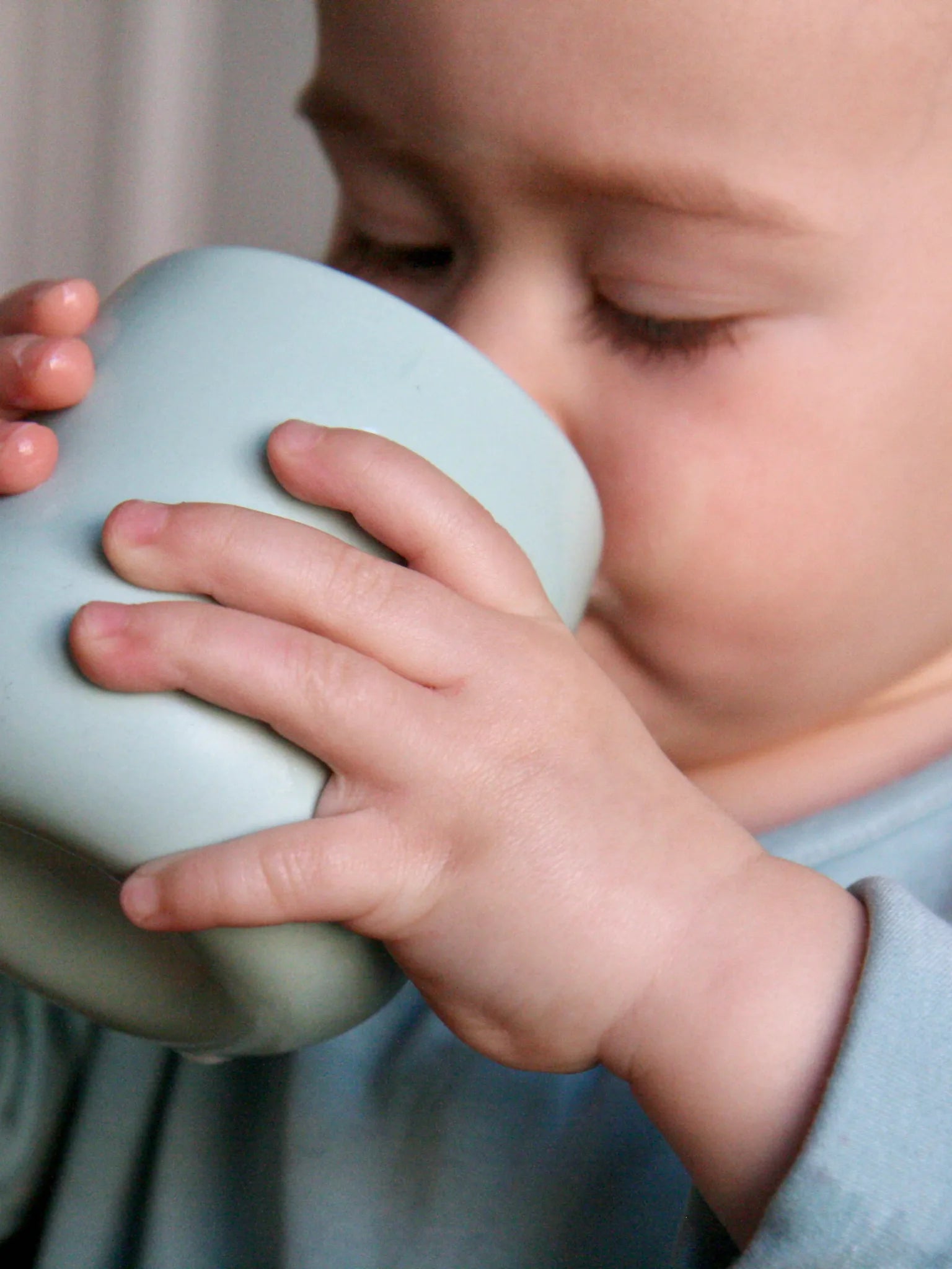 Kind mit Becher aus Porzellan in der Hand, in der Farbe Agave, Detailansicht.