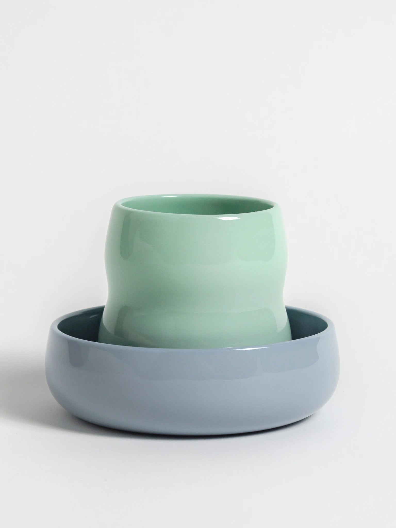 Kindergeschirr aus Porzellan; Kinderbecher in der Farbe Agave und Kinderschale in Kornblume ineinander gestapelt.