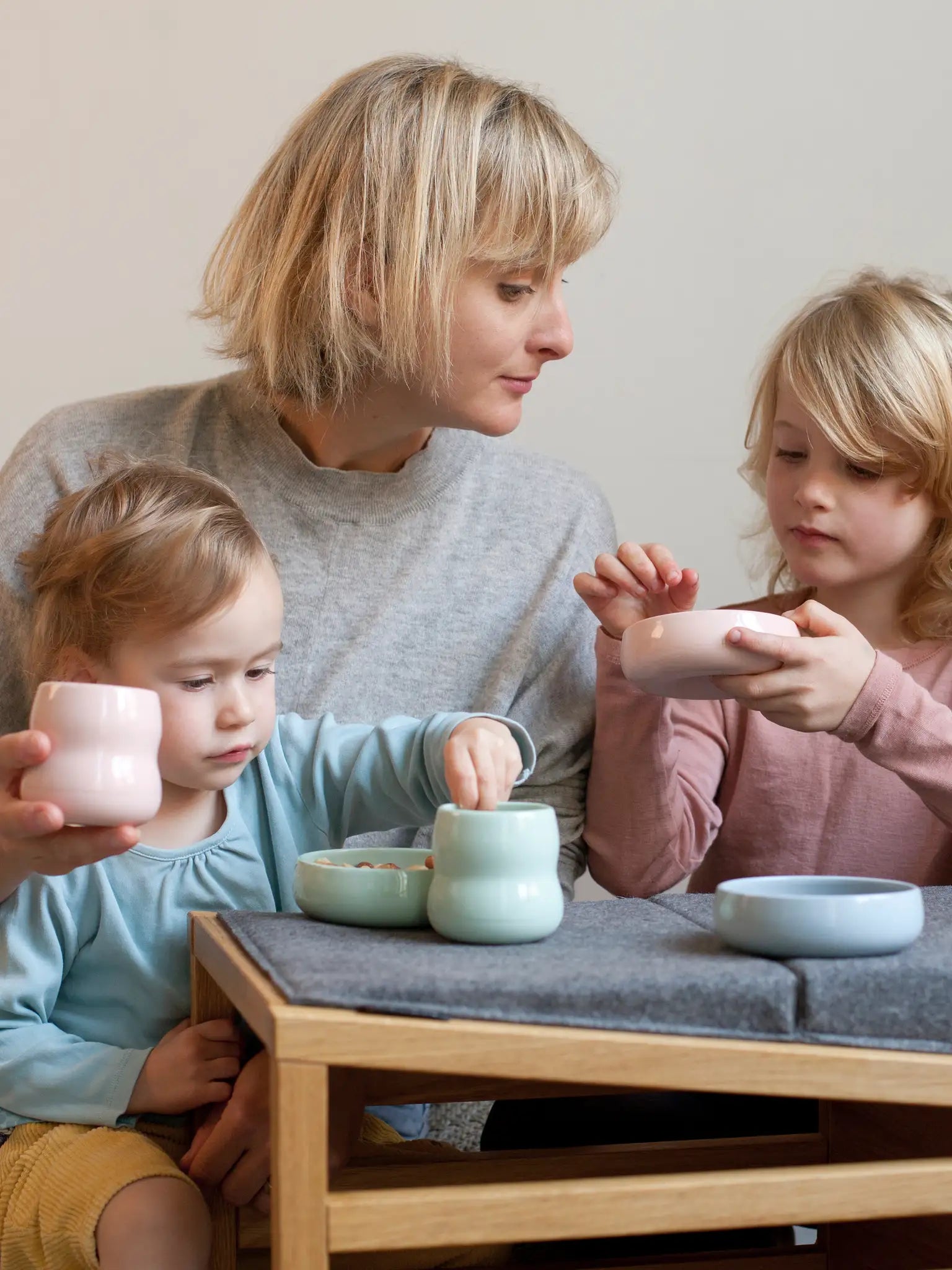 Mutter mit Kindern und Kindergeschirr aus Porzellan; Kinderbecher in der Farbe Agave und Rosé mit Schalen in Rosé, Kornblume und Agave.