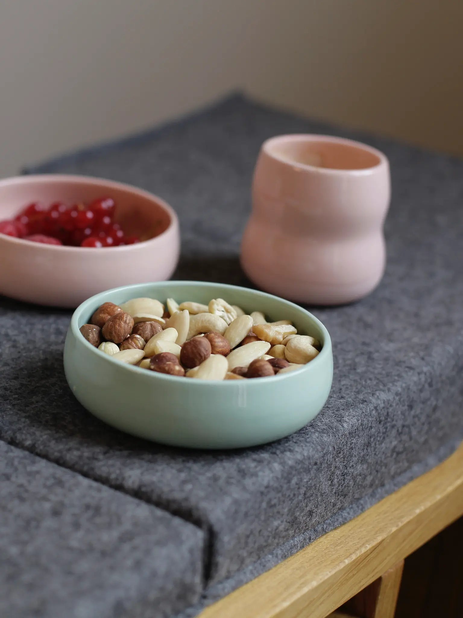 Kindergeschirr aus Porzellan; Kinderbecher in der Farbe Rosé und Schalen in Agave und Rosé gefüllt mit Früchten und Nüssen.