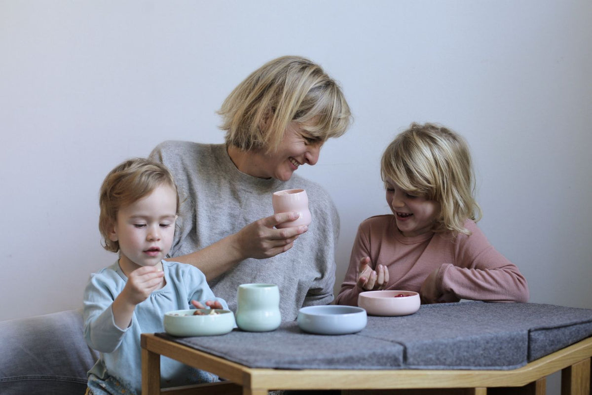 Mutter und Kinder sitzen am ZAUNKÖNIG® als Tischchen mit Kindergeschirr aus Porzellan