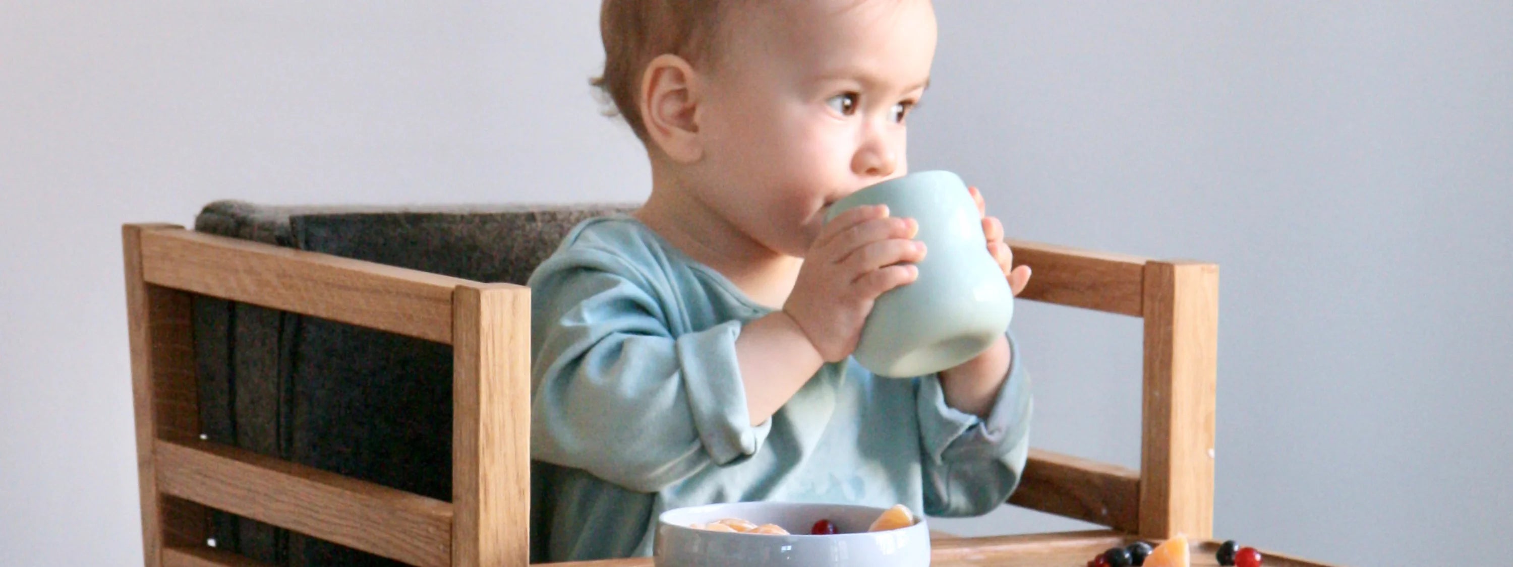 Kind mit Becher aus Porzellan in den Händen; Kinderbecher in der Farbe Agave.