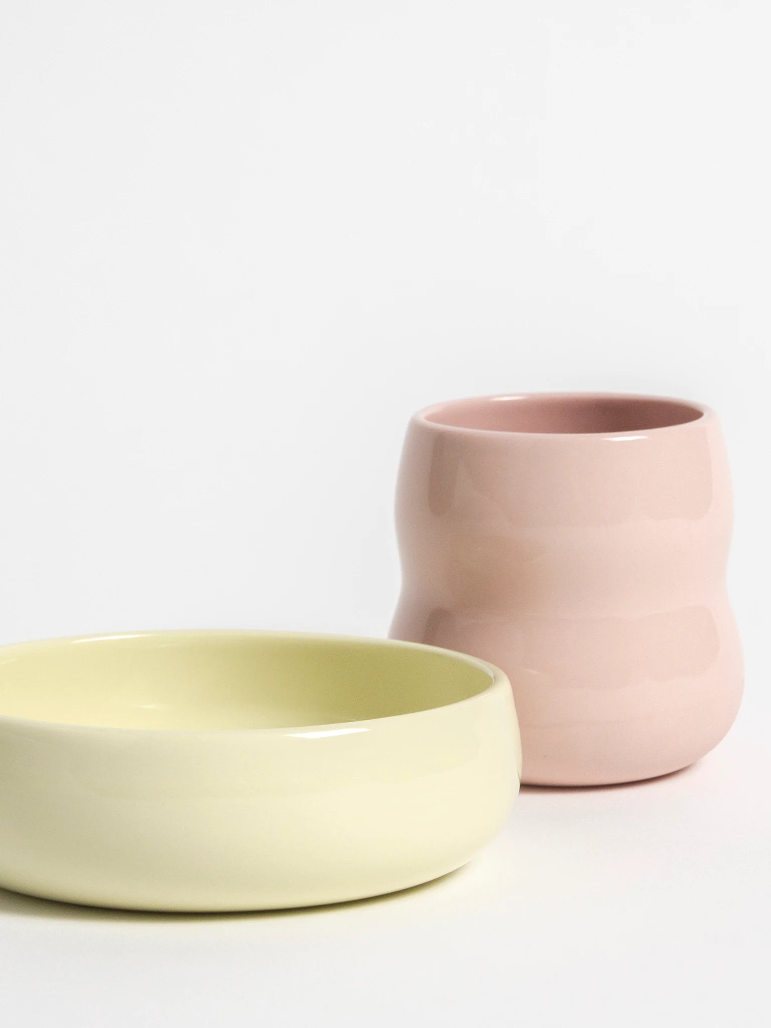 Das ZAUNKÖNIG Kindergeschirr aus Porzellan, Frontansicht des Kinderbechers in Rosé und der Kinderschale in Limone.