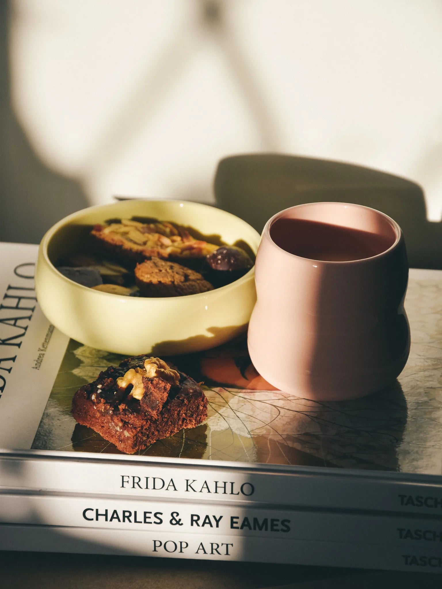 Kindergeschirr aus Porzellan auf Büchern, Frontansicht des Kinderbechers in Rosé und der Kinderschale in Limone gefüllt mit Plätzchen.