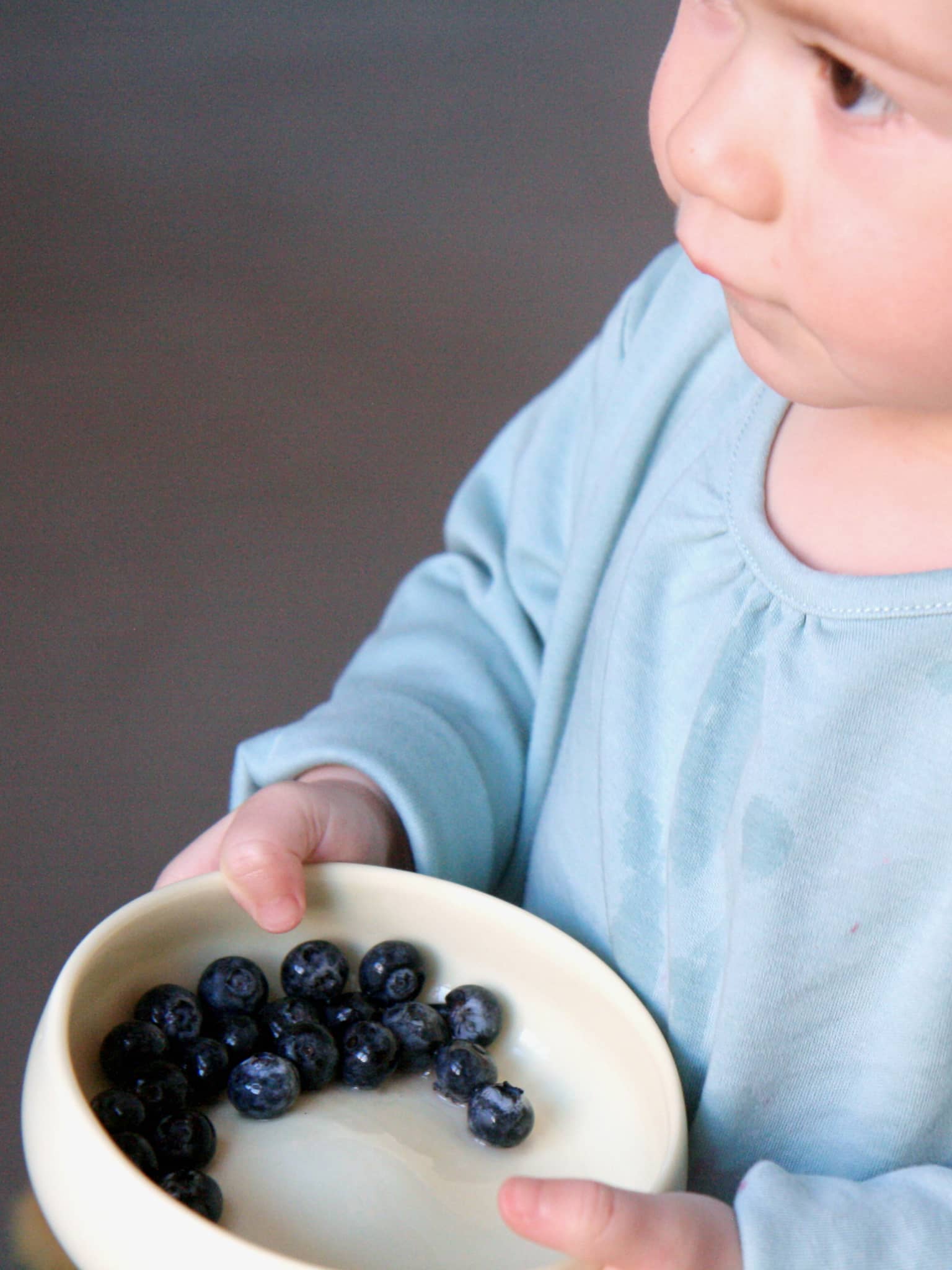 Kind mit Kindergeschirr aus Porzellan in der Hand; Kinderschale in der Farbe Limone gefüllt mit Beeren.