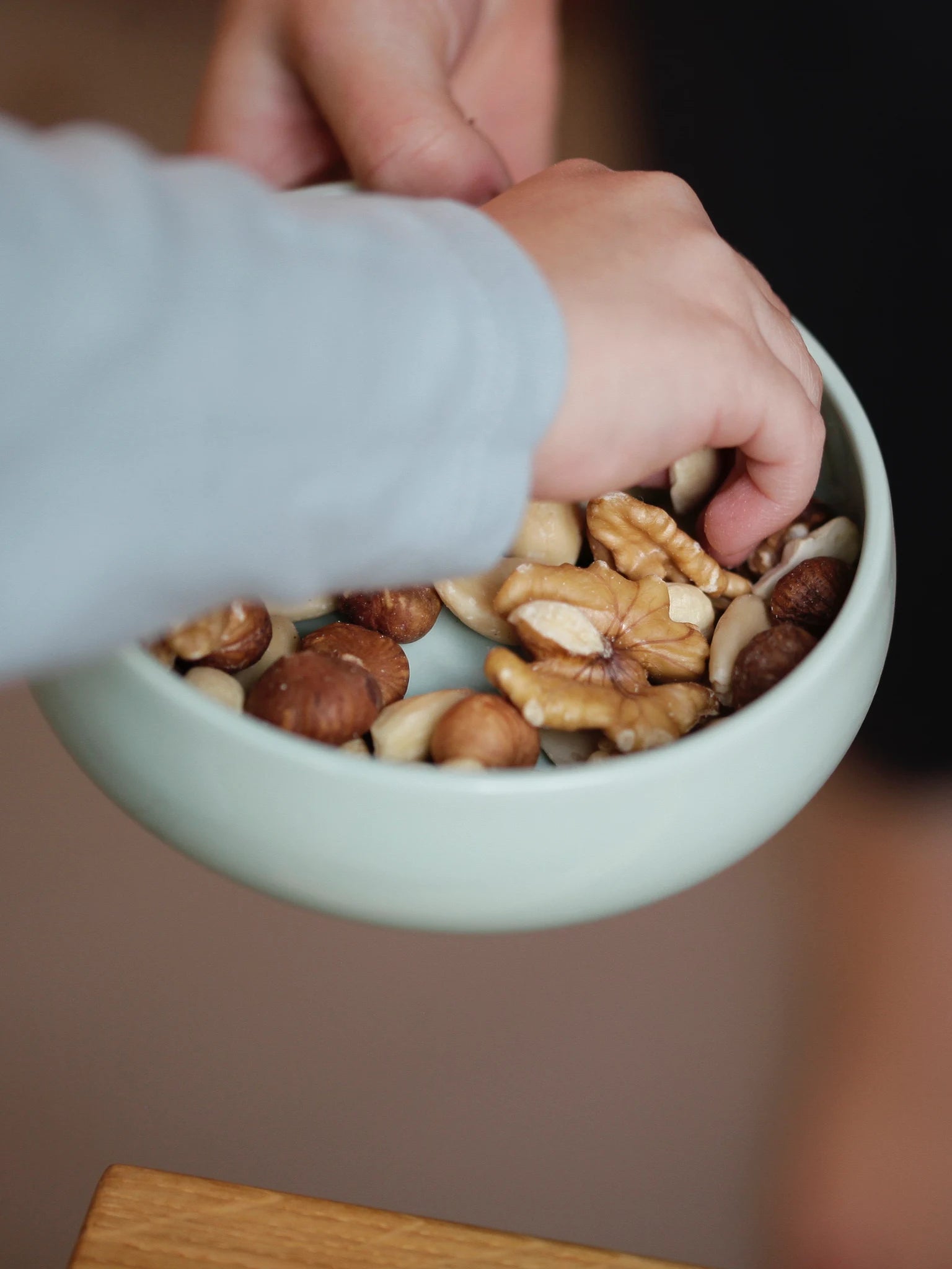 Porzellangeschirr für Kinder; Kinderschale in der Farbe Agave gefüllt mit Nüssen; Frontansicht mit Kinder, das Nüsse aus der Schale greift.