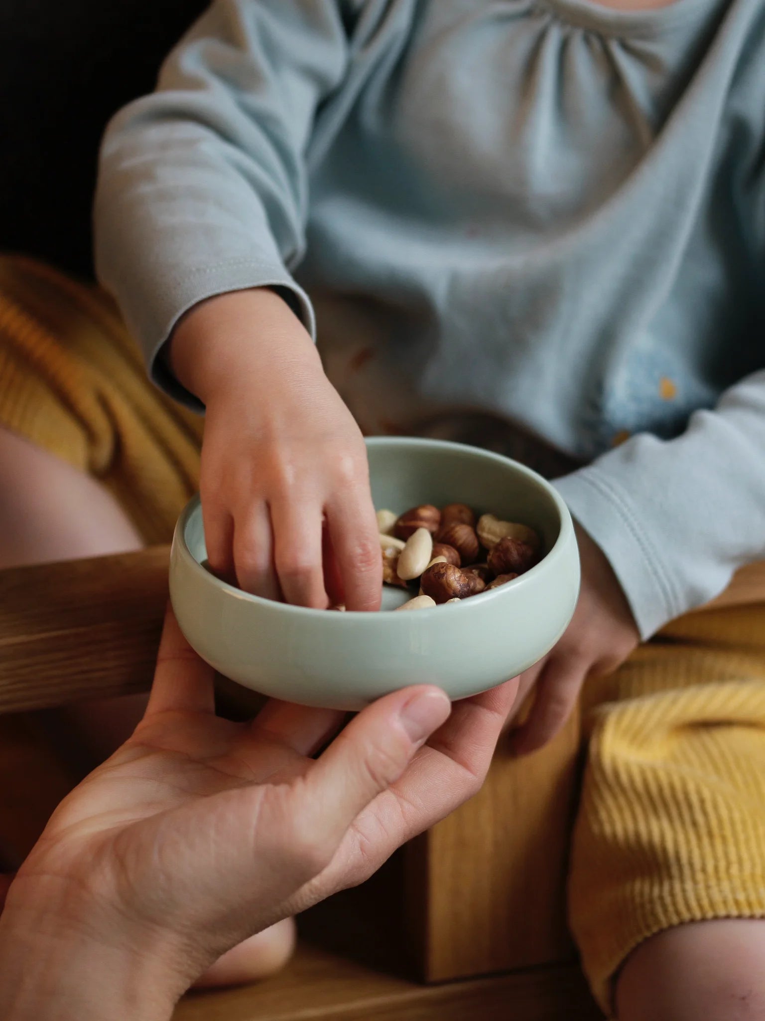 Kindergeschirr aus Porzellan; Kinderschale in der Farbe Agave; Frontansicht mit Kind und Hand der Mutter, die Schale hält.