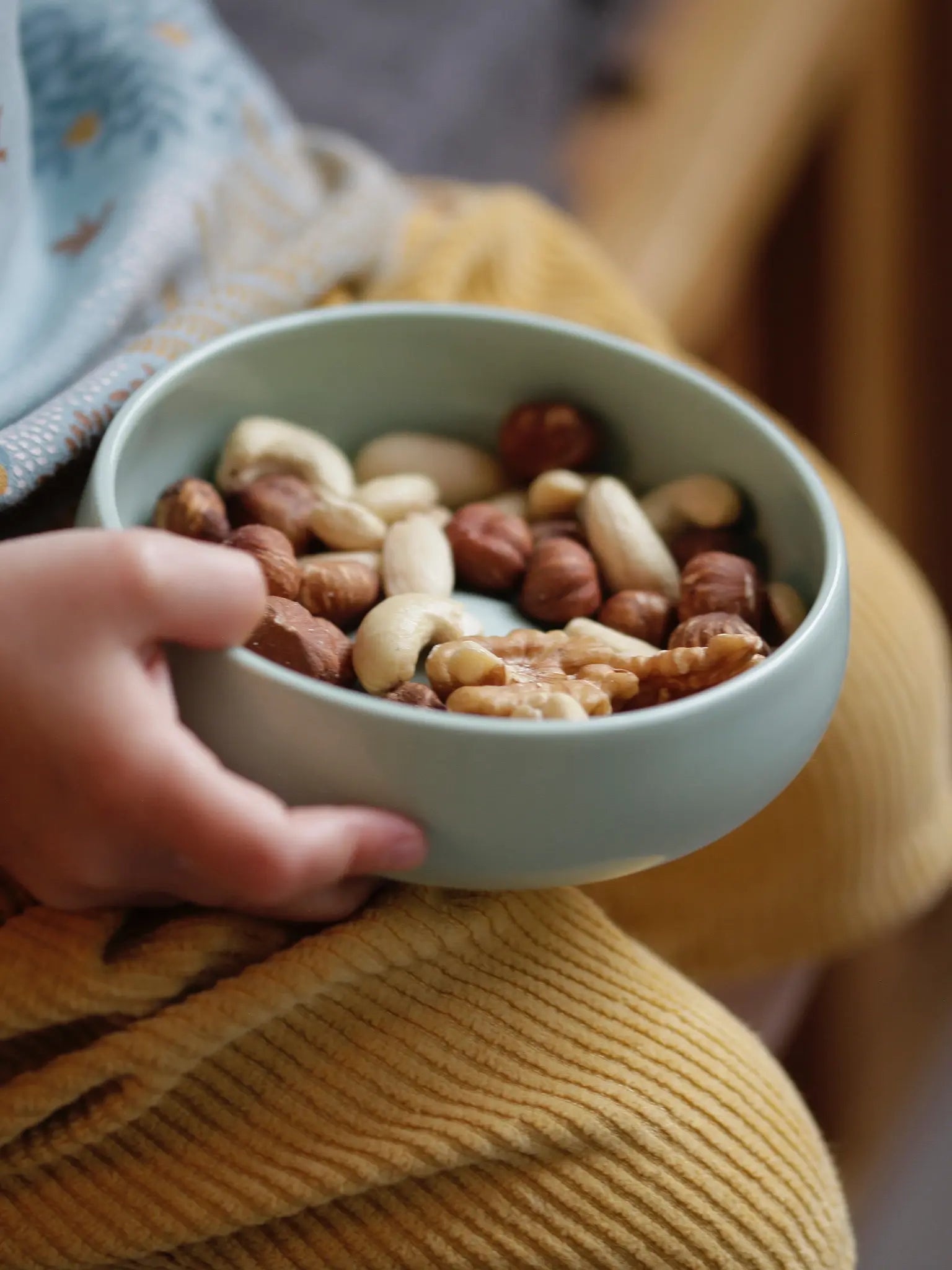 Schale aus Porzellan in einer Kinderhand in der Farbe Agave mit Nüssen gefüllt.