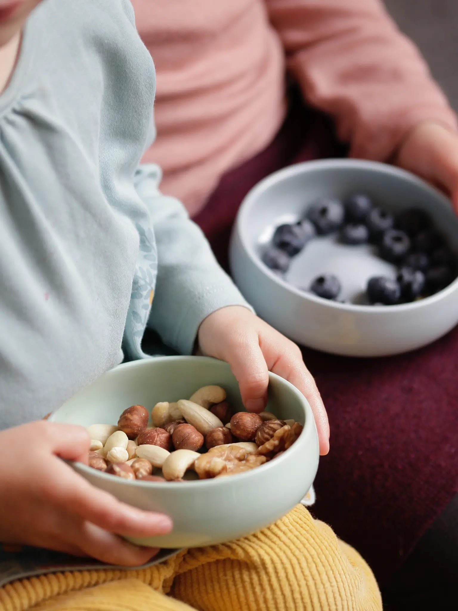 Kinder mit Geschirr aus Porzellan in den Händen; Kinderschalen in den Farben Kornblume und Agave.