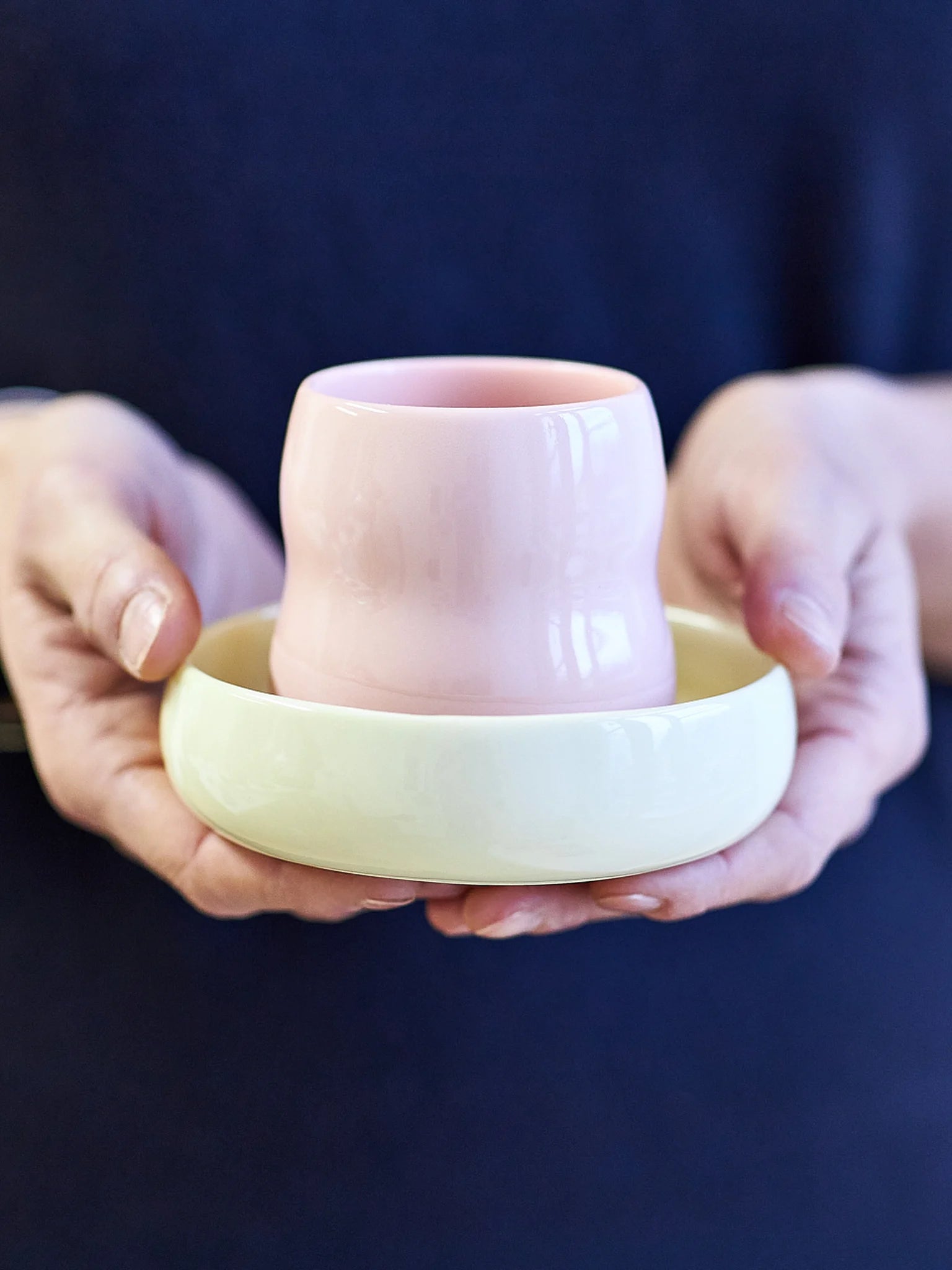 Das Kindergeschirr aus Porzellan von ZAUNKÖNIG, Frontansicht des Kinderbechers in Rosé und der Kinderschale in Limone in den Händen einer Erwachsenen.