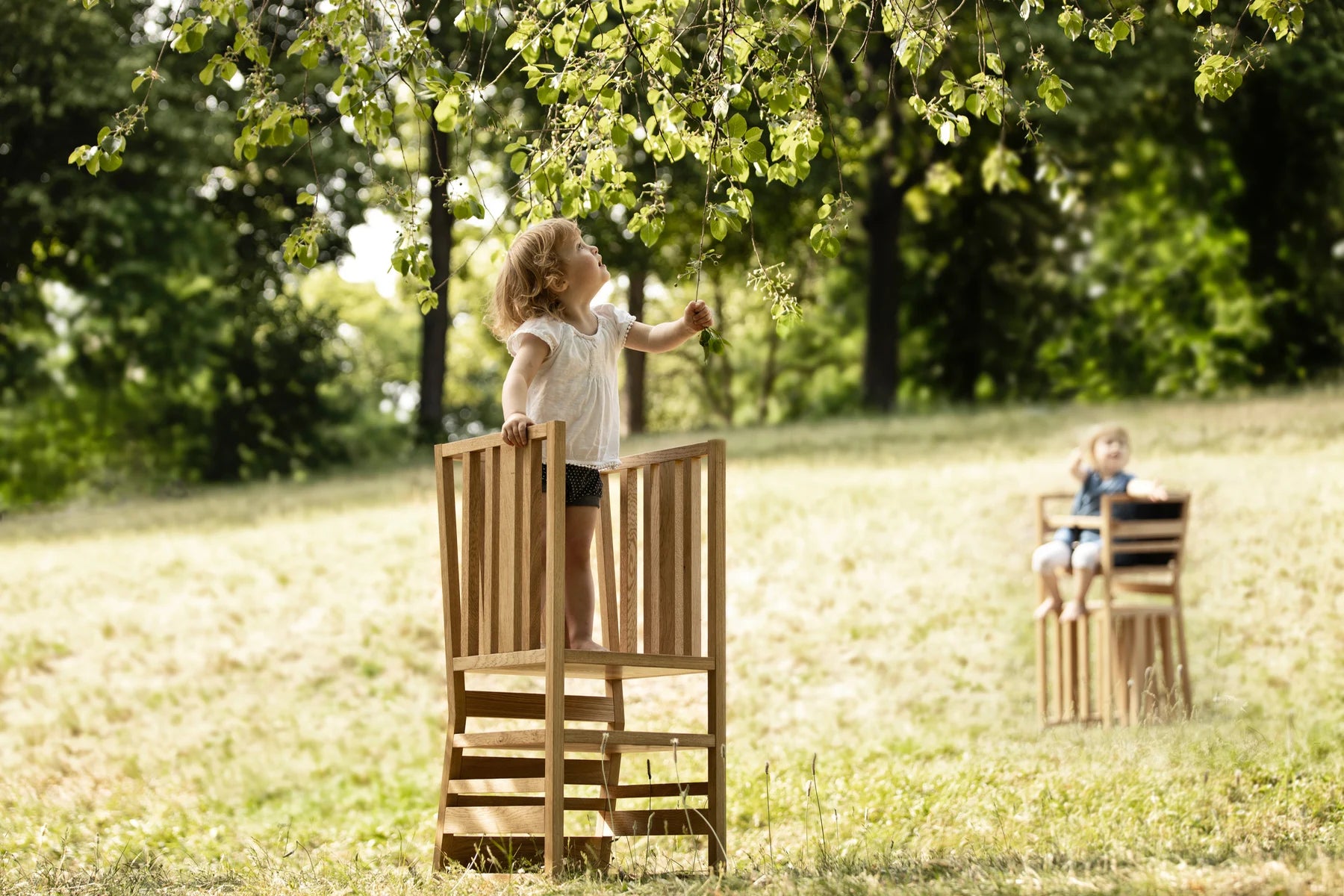 Der ZAUNKÖNIG Lernturm (3-in-1) aus massivem Eichenholz im Wald; Seitenansicht mit Kind.