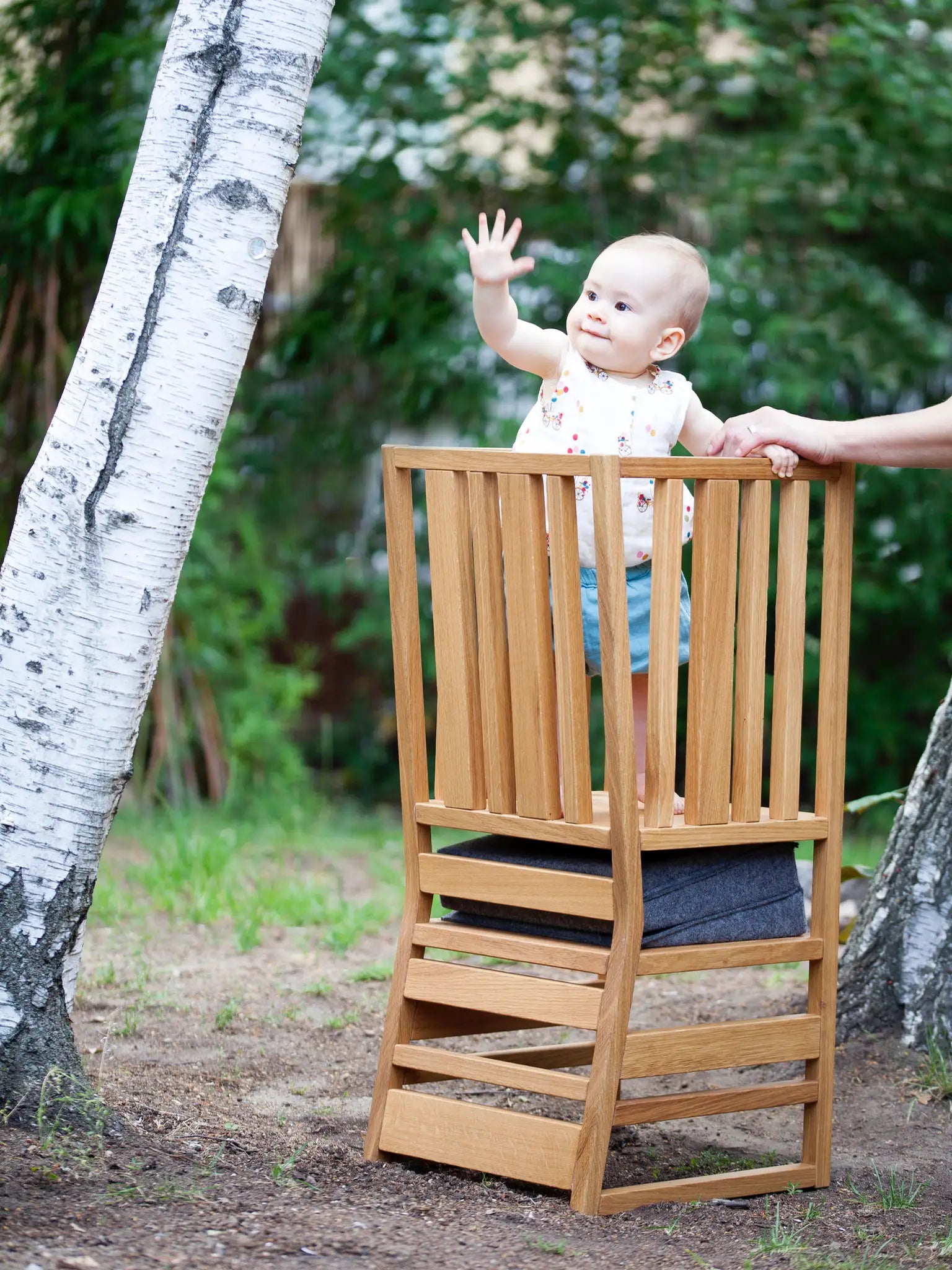 Der ZAUNKÖNIG Lernturm (3-in-1) aus massivem Eichenholz im Garten, Seitenansicht mit Baby, das darauf steht.