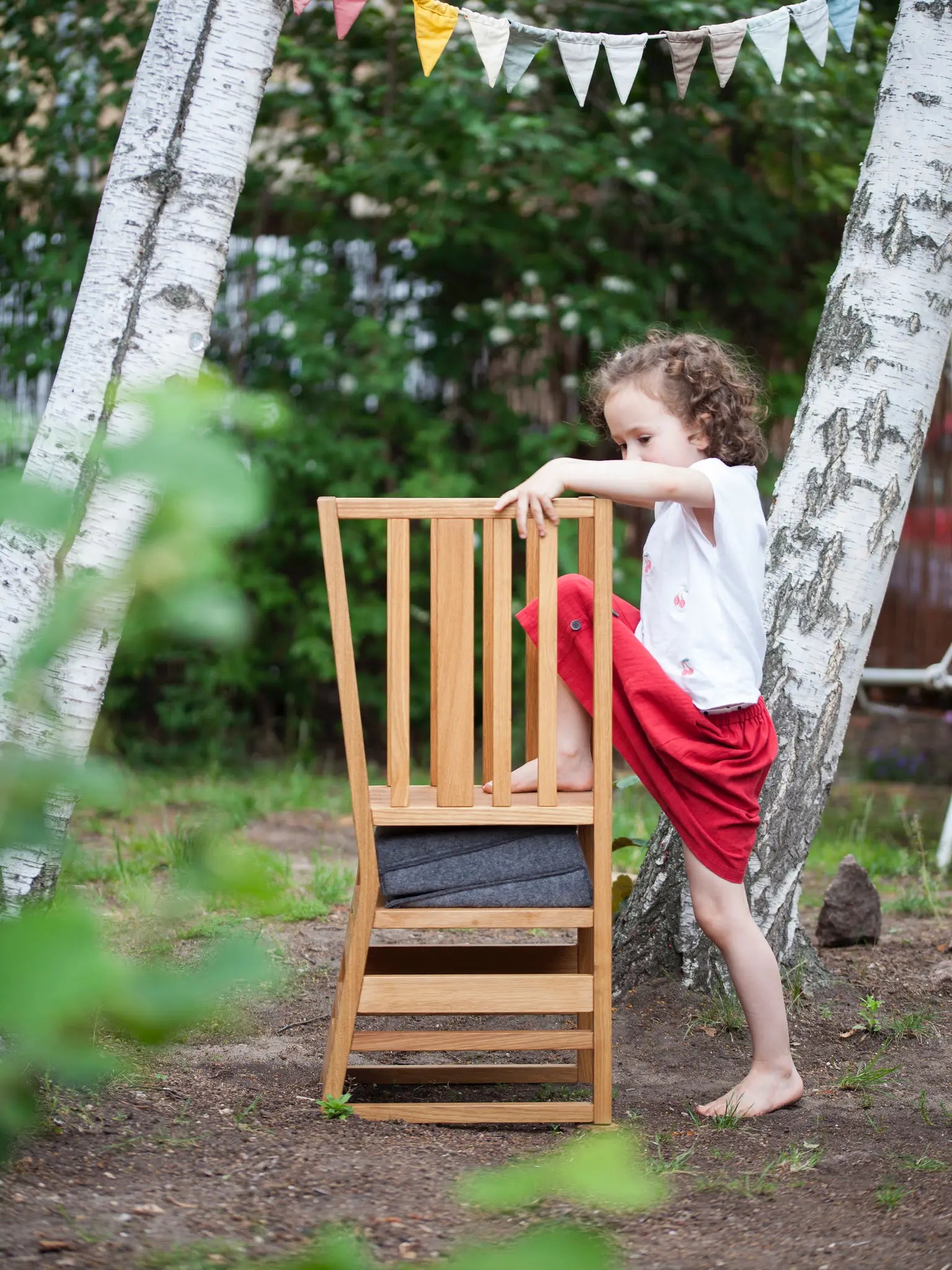 Der ZAUNKÖNIG Lernturm (3-in-1) aus massivem Eichenholz im Garten; Seitenansicht mit Kind, das eigenständig aufsteigt.