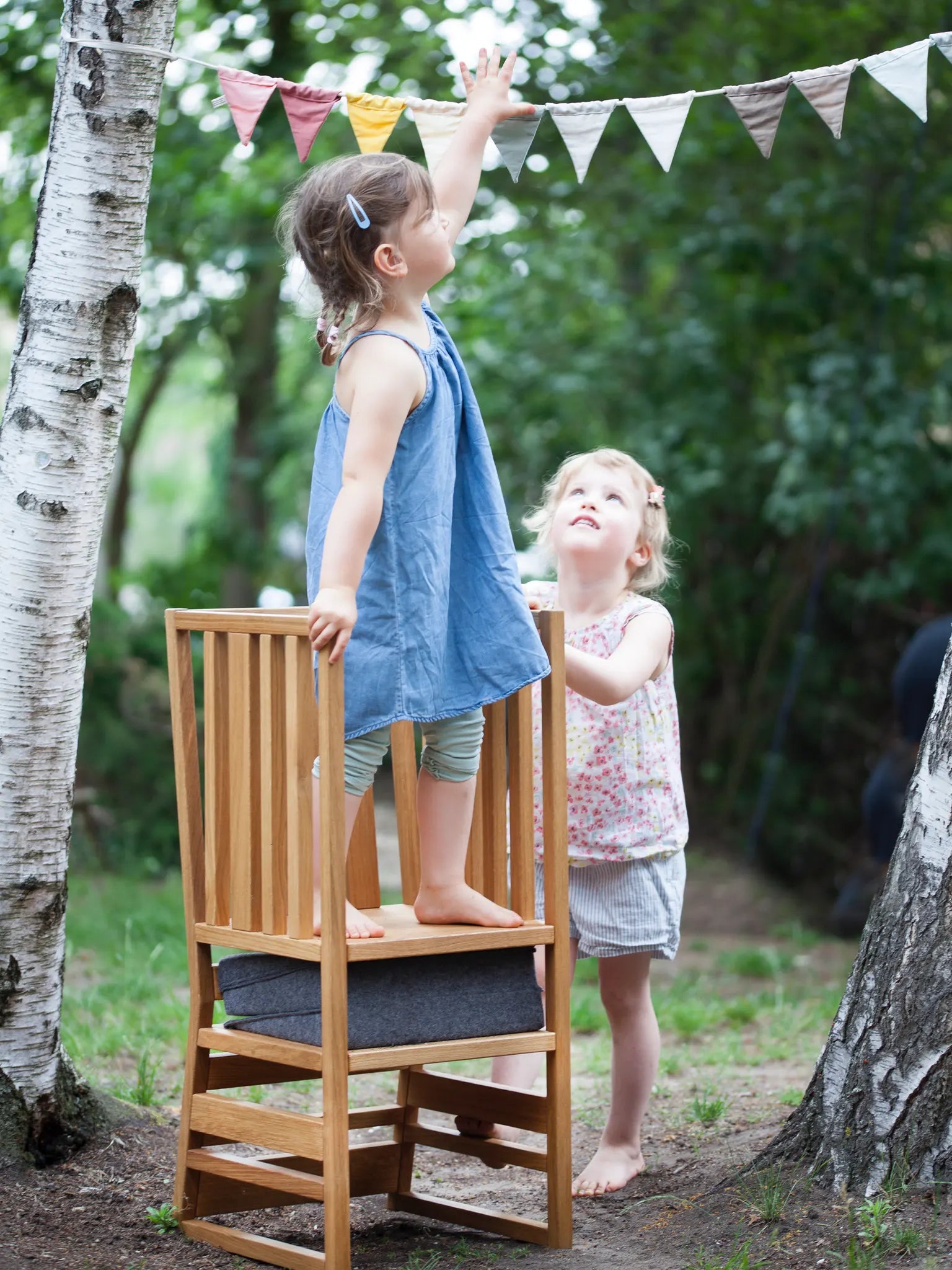 Der ZAUNKÖNIG Lernturm (3-in-1) aus massivem Eichenholz im Garten mit Faltpolster aus Wollfilz; Frontansicht mit Kindern, die spielen.