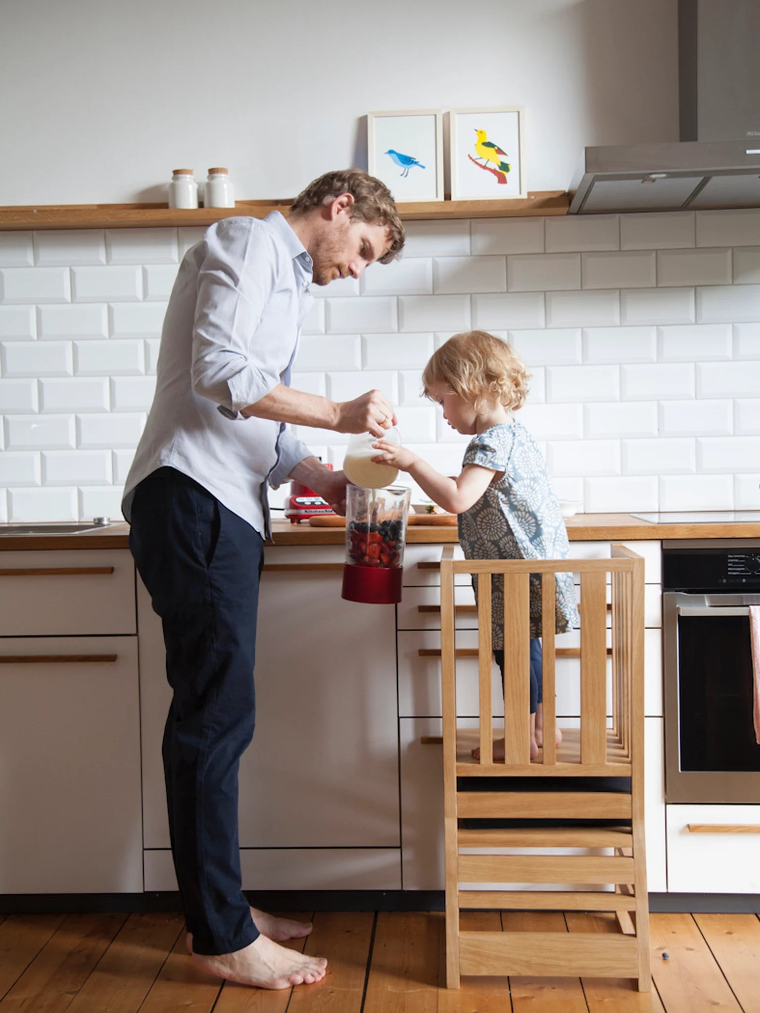 Der ZAUNKÖNIG Lernturm (3-in-1) aus massivem Eichenholz in der Küche als Küchenhelfer; Rückansicht mit Kind und Vater, die zusammen kochen.