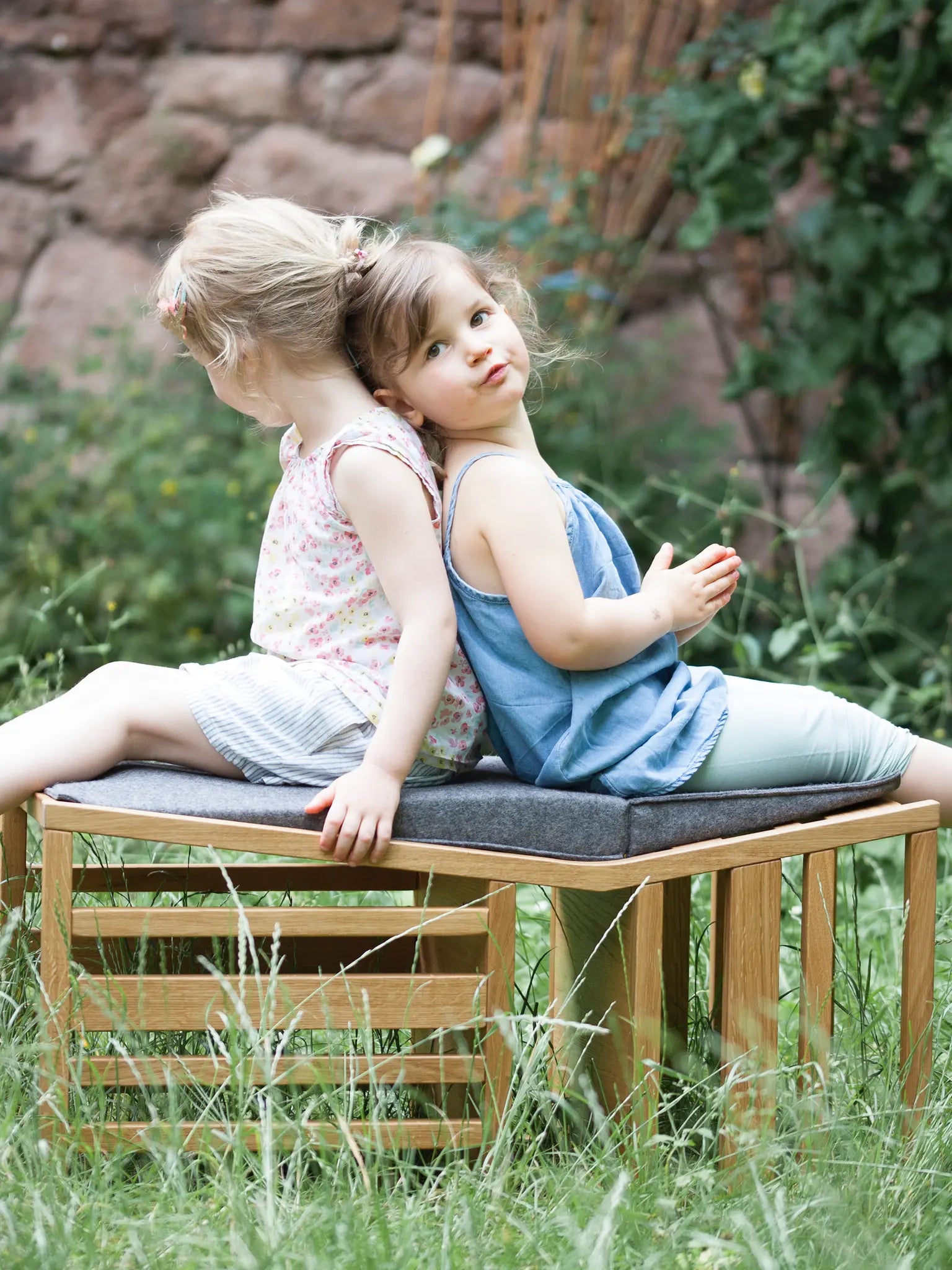 Der ZAUNKÖNIG Lernturm (3-in-1) aus massivem Eichenholz als Sitzbank im Garten; Frontansicht mit zwei Kindern, die darauf sitzen.