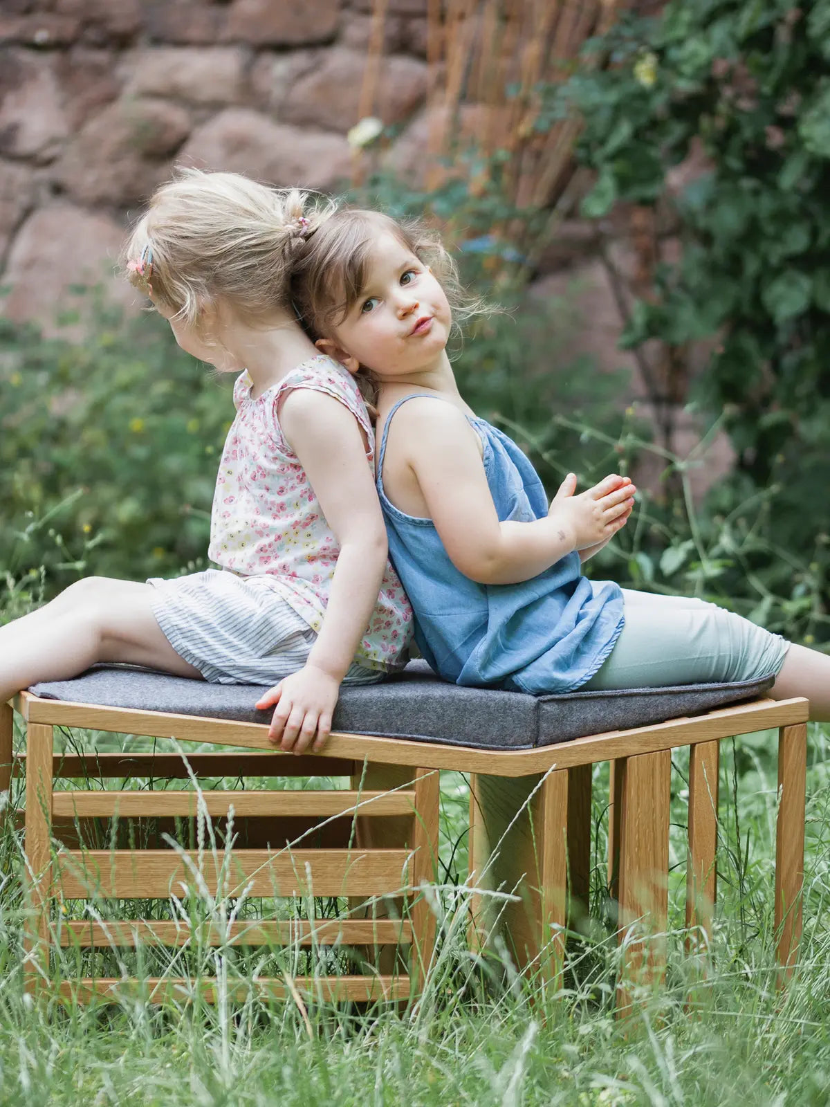 Der ZAUNKÖNIG Lernturm (3-in-1) aus massivem Eichenholz als Sitzbank im Garten; Frontansicht mit zwei Kinder, die darauf sitzen.