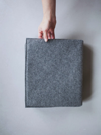 Eine Hand hält das ZAUNKÖNIG® Faltpolster aus Wollfilz in der Farbe Elephant Grey