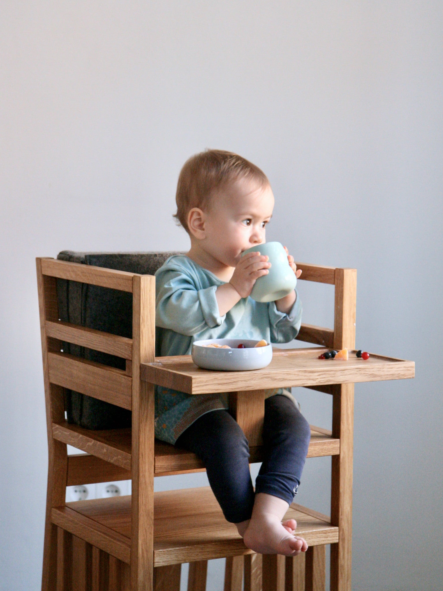 Kind sitzt im ZAUNKÖNIG® als Hochstuhl und trinkt aus dem Kinderbecher aus Porzellan