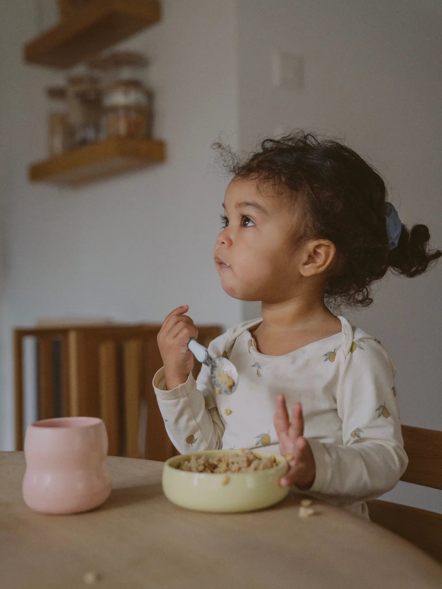 Ein Kind sitzt am Küchentisch und isst aus der Kinderschüssel aus Porzellan. 